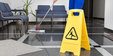 person mopping the floor next to a slippery floor sign