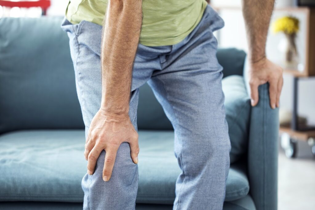 man clutching knee in pain in living area